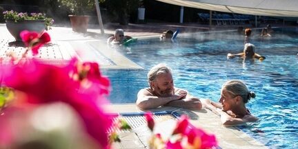 Wohlfühltherme Bad Griesbach Wohlfühltherme Bad Griesbach - Paar im Wasser im Außenpool mit Blüten im Vordergrund